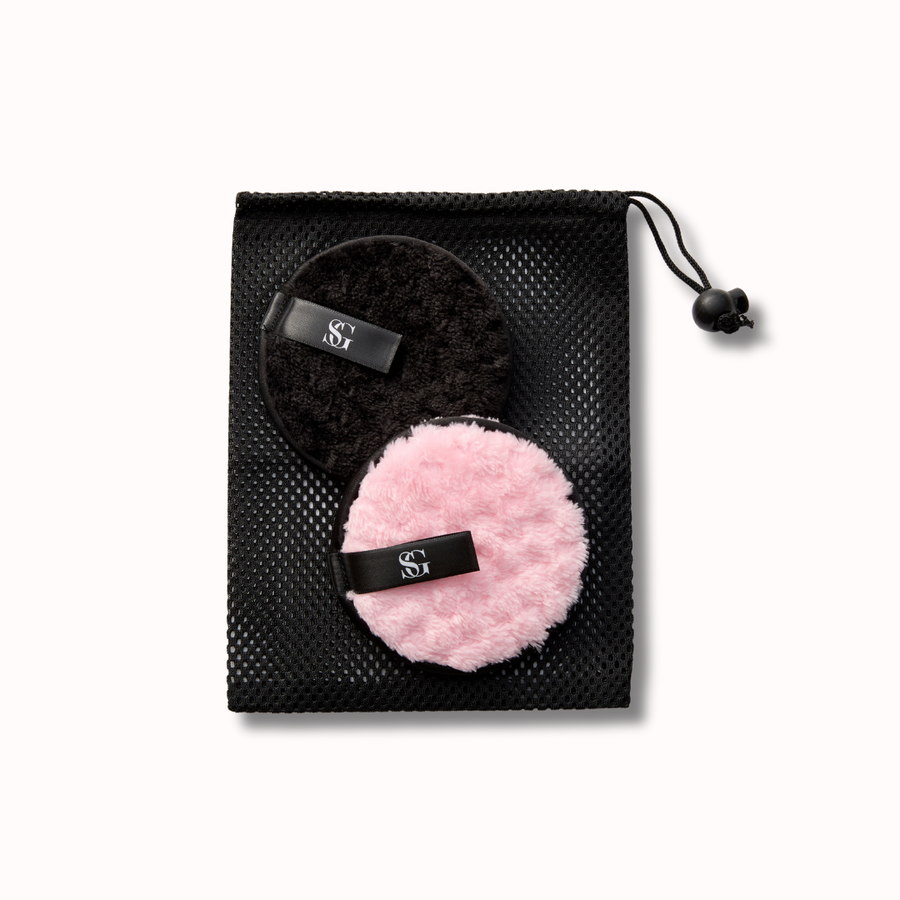 Black drawstring bag with a black and a pink reusable makeup remover puff on a white background