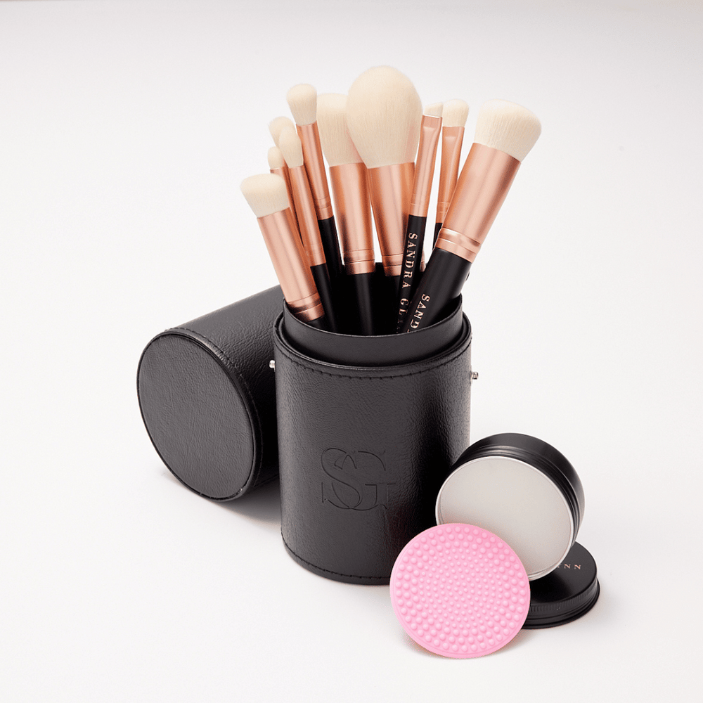 Rose gold brushes in black brush holder with brush soap tin on white background