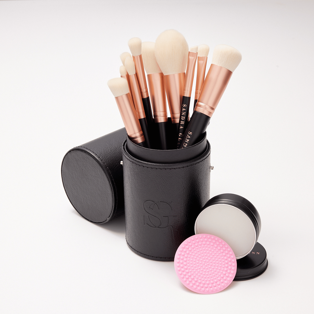 Rose gold brushes in black brush holder with brush soap tin on white background