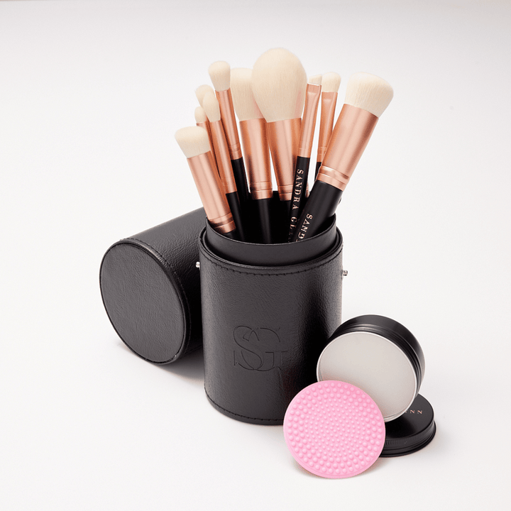 Rose gold brushes in black brush holder with brush soap tin on white background